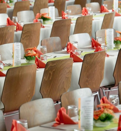 Beautifully arranged tables with wooden chairs for a formal event, adorned with orange flowers.